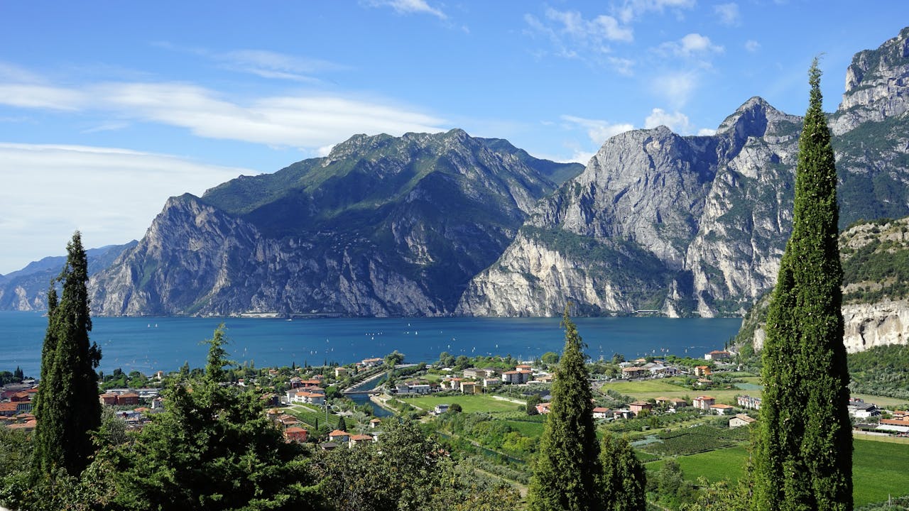 Scenic view of Lake Garda with surrounding mountains and lush green trees in the foreground.