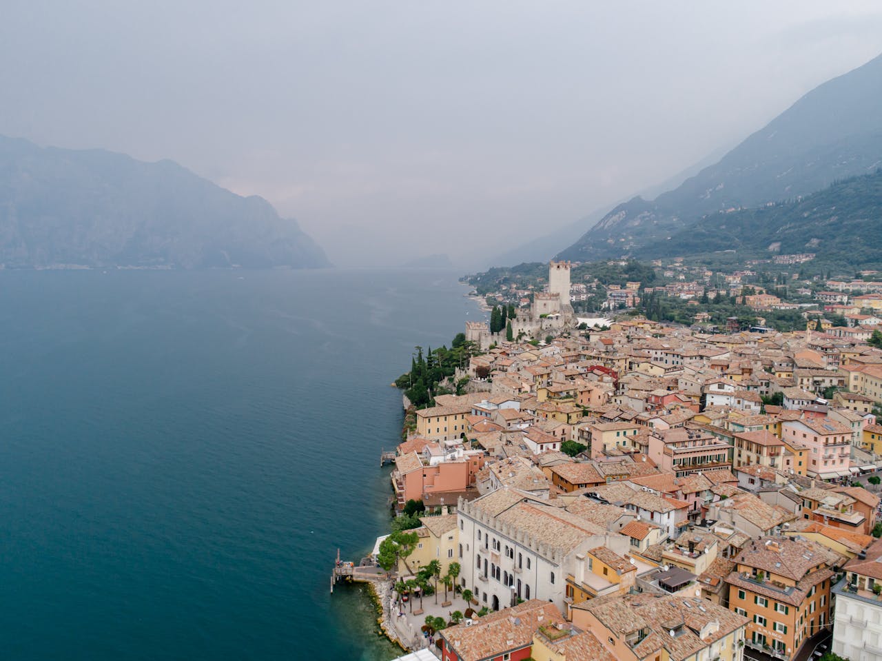 Scenic aerial view of Malcesine by Lake Garda with mountains in the background on a foggy day.